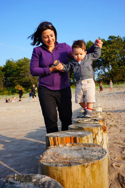 SIANOZETY, POLAND - Jul 21, 2015: SIANOZETY, Woman holding young child while walking on wooden poles at the beach - Foto, immagini