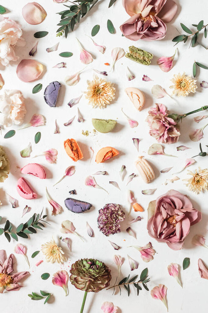 A flat lay composition with multicolored French macaroons and flowers on a white background - Photo, image