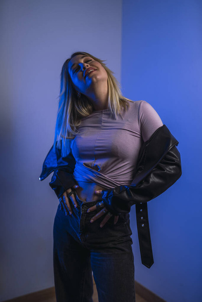 An attractive Caucasian female from Spain in a leather jacket posing in a studio with blue lights - Φωτογραφία, εικόνα