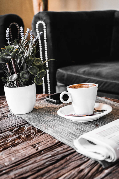 A vertical shot of a cup of fresh morning coffee and a potted plant on a table - 写真・画像