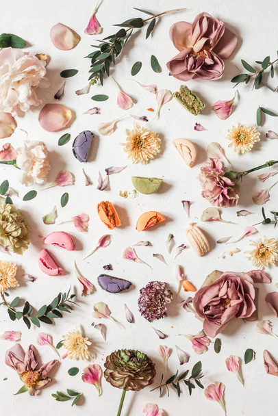 A flat lay composition with multicolored French macaroons and flowers on a white background - Photo, image