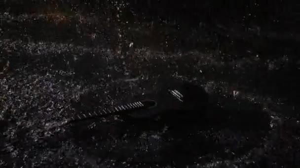 Top view wooden acoustic guitar hits the surface of water, creating a lot of splashes. Musical instrument in the rain. Guitar among the raindrops on a black studio background. Close up. Slow motion. - Filmmaterial, Video