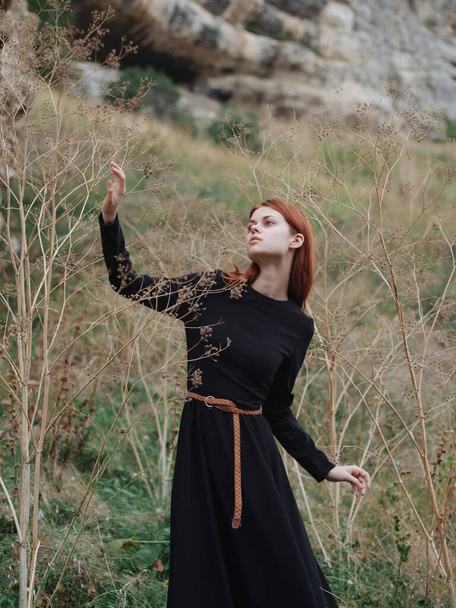Red-haired Woman in a black dress are walking on nature in autumn in the forest - Фото, зображення