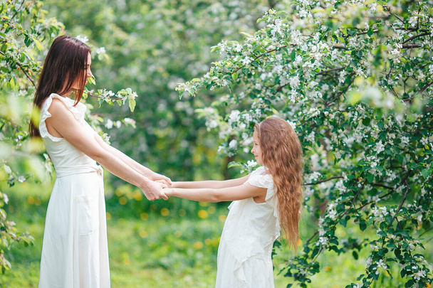 Entzückendes kleines Mädchen mit junger Mutter im blühenden Kirschgarten an einem schönen Frühlingstag - Foto, Bild