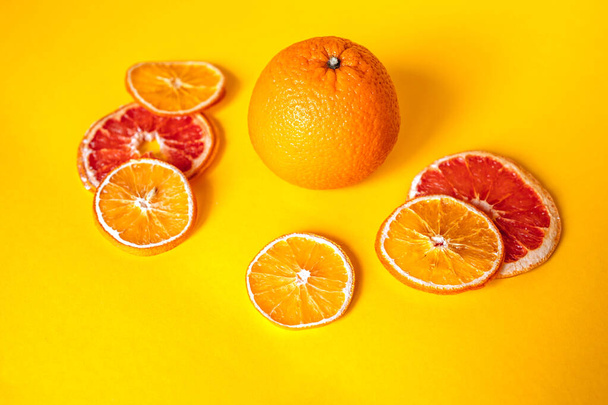 Σύνθεση με ξηρά πορτοκάλια και ολόκληρα φρούτα σε πορτοκαλί φόντο - Φωτογραφία, εικόνα