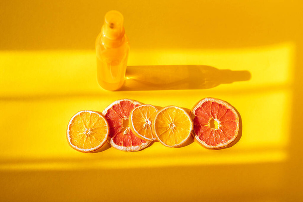 Бутылка спрея с сухими апельсинами на оранжевом фоне и оконный свет - Фото, изображение