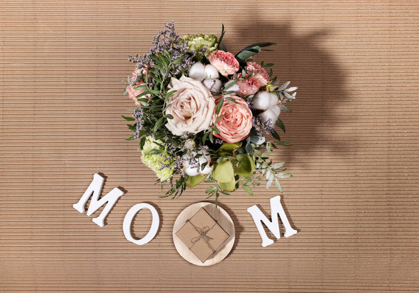 Festive composition for Mothers day with flowers bouquet, white letters MOM, diy gift box on beige cardboard backdrop. - Photo, Image