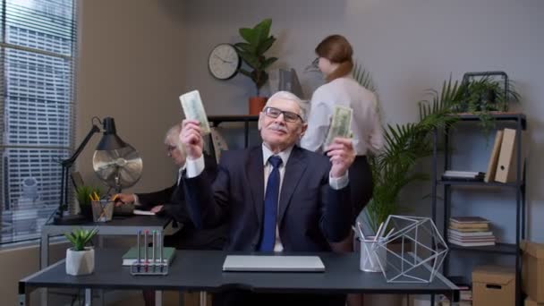 Starszy człowiek szef świętuje sukces w biznesie tańcząc z pieniędzmi gotówką w nowoczesnym pokoju biurowym - Materiał filmowy, wideo