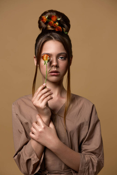 Portrait of a teenage girl. In the hair of the rose. She is holding a flower near the oits. One eye covers the bud. Bronze colors. - Foto, immagini