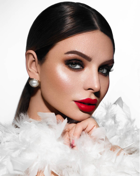 Portrait of a woman. The beauty. Professional makeup. Long eyelashes. Red lipstick. Shawl made of white feathers. Brunette. - Foto, Imagem
