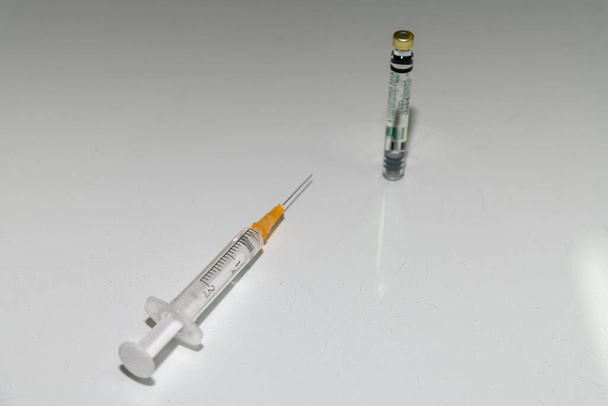 Seringue et aiguille avec une dose de vaccin. Canette de vaccin contre Corona, gros plan sur une table blanche. - Photo, image