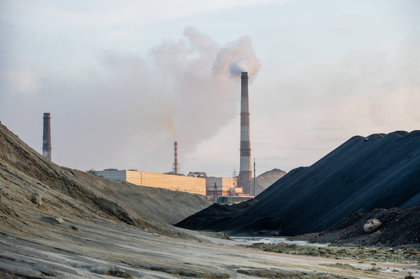 A szennyezett dombok és az ipari gyárak közötti szennyezett utak és nagy pocsolyák vagy folyó látványa mérgező füstöt bocsát ki a felhős ég ellen - Fotó, kép