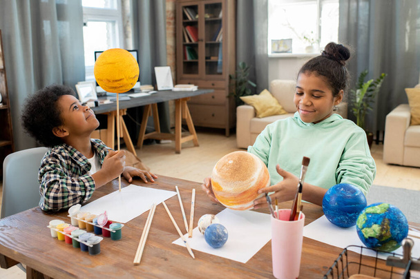 Dos adorables niños de escuela primaria de raza mixta haciendo planetas mientras se preparan para la lección de astronomía por mesa en el ambiente hogareño - Foto, imagen