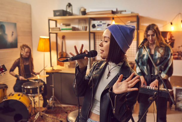 Young woman in stylish clothing singing in microphone with her musical group in the background - Foto, immagini