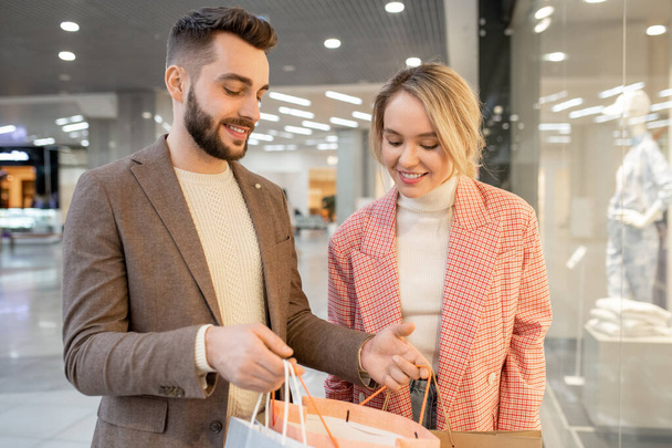 Młoda szczęśliwa para spoglądająca w torby na zakupy i zadowolona z zakupów - Zdjęcie, obraz