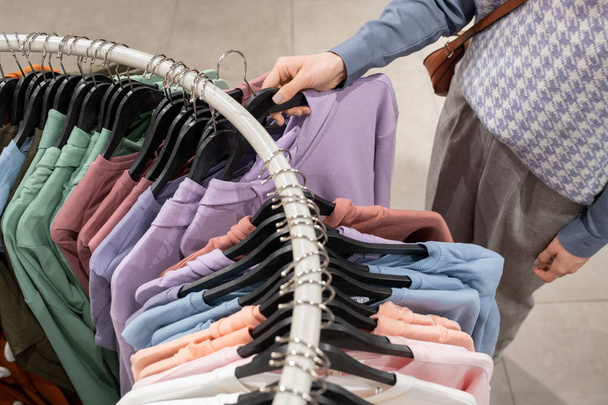 Close-up of woman choosing shirt on the rack for herself in clothing store - Photo, Image