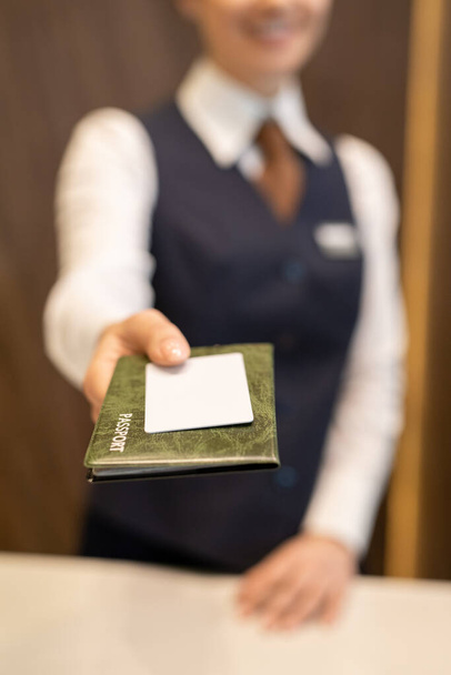 フロントカメラの前に立つ制服姿の若い女性受付嬢の手と受付カウンター越しにホテルのゲストにパスポートを渡す - 写真・画像