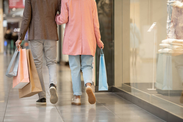 Visão traseira do jovem casal com sacos de compras andando ao longo do shopping - Foto, Imagem