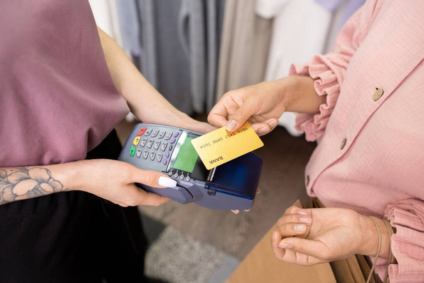 Κοντινό πλάνο νεαρής γυναίκας που πληρώνει με πιστωτική κάρτα για τις αγορές της στο κατάστημα - Φωτογραφία, εικόνα