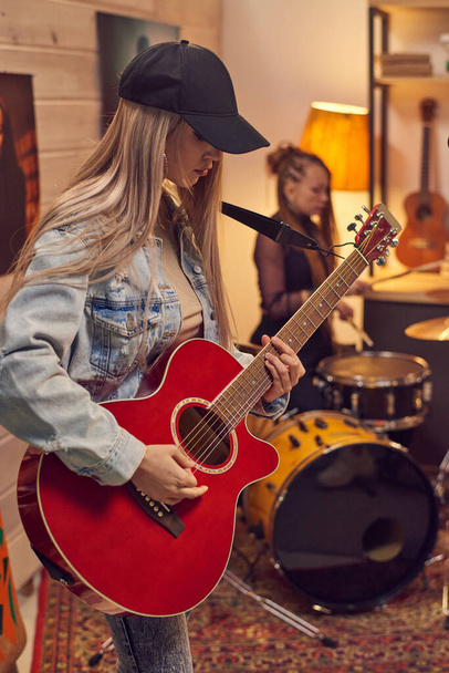 Νεαρή γυναίκα κιθαρίστρια που παίζει ηλεκτρική κιθάρα με το μουσικό της συγκρότημα στο στούντιο - Φωτογραφία, εικόνα