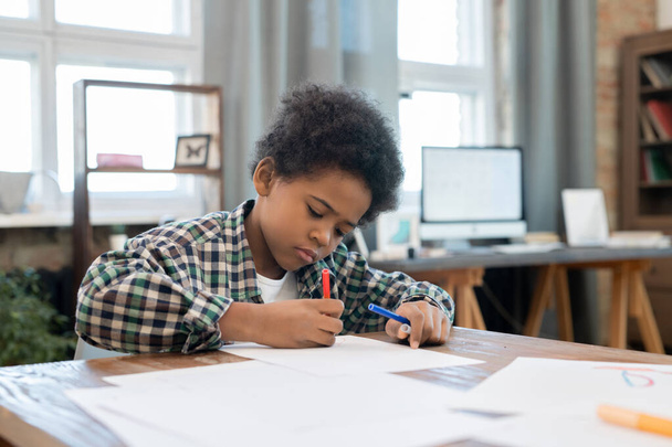 Huolellinen koulupoika casualwear piirustus korostajilla paperilla pöydällä olohuoneessa nauttien vapaa-ajasta kotitehtävien jälkeen - Valokuva, kuva
