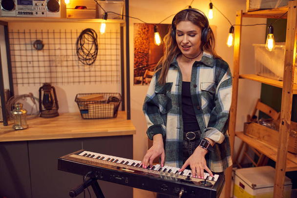 Young musician in headphones playing on electric piano in the studio - Photo, Image