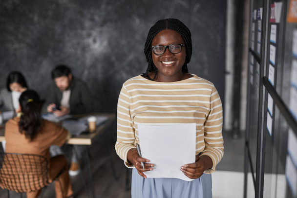 Waist up portrait of smiling African-American businesswoman standing by glass wall while planning project in modern office, copy space - Zdjęcie, obraz