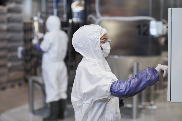 Zijaanzicht portret van vrouwelijke werknemer in beschermende kleding tijdens het gebruik van apparatuur in chemische fabriek, kopieerruimte - Foto, afbeelding