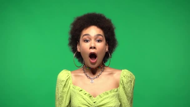 Langzame beweging van opgewonden en glimlachende Afrikaanse Amerikaanse vrouw geïsoleerd op groen  - Video