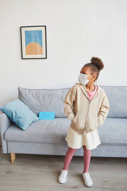 Retrato vertical de larga duración de una niña afroamericana despreocupada que llevaba máscara en casa el día de los padres y mirando hacia otro lado, espacio para copiar - Foto, imagen