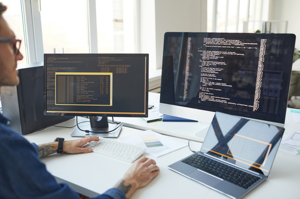 Вид збоку на чоловічий програміст, що пише код під час використання декількох комп'ютерів в офісі розробників ІТ, копіювання простору
 - Фото, зображення