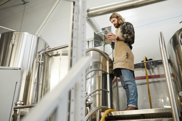 Полнометражный портрет бородатого пивовара, контролирующего производство на пивоваренном заводе, копировальное пространство - Фото, изображение