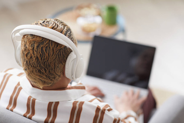 Blick auf moderne Frau, die Kopfhörer trägt, während sie zu Hause Laptop benutzt, Kopierraum - Foto, Bild