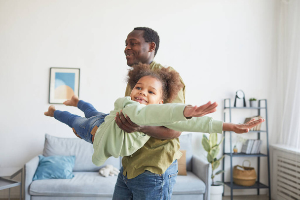 Retrato de un hombre afroamericano juguetón jugando con una linda hija en el interior del hogar mínimo, espacio para copiar - Foto, Imagen