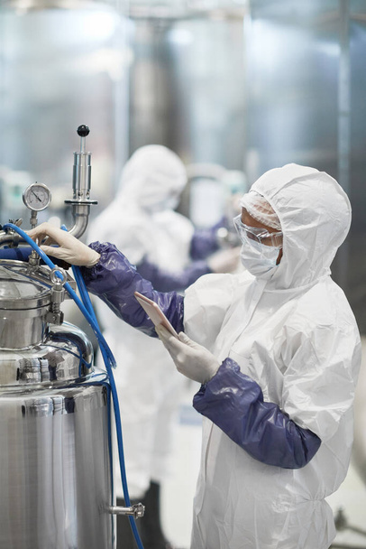 Retrato vertical de una trabajadora vestida con traje protector mientras opera equipo en planta química moderna, espacio para copiar - Foto, Imagen