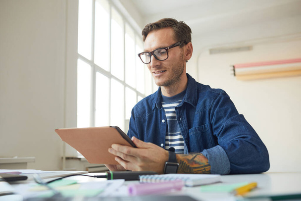 Portrait of contemporary tattooed man using digital tablet while working at desk office, male designer or photographer concept, copy space - Photo, Image