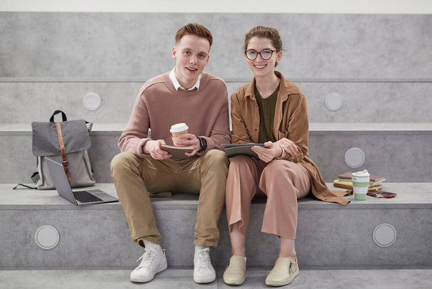 Vorderseite Porträt von zwei lächelnden jungen Menschen, die in die Kamera schauen, während sie im Aufenthaltsraum in der College-Halle sitzen, Kopierraum - Foto, Bild