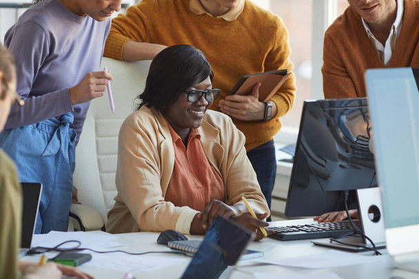 Cropped shot of diverse IT development team collaborating on project with smiling African-American woman using computer in software production studio - Photo, Image