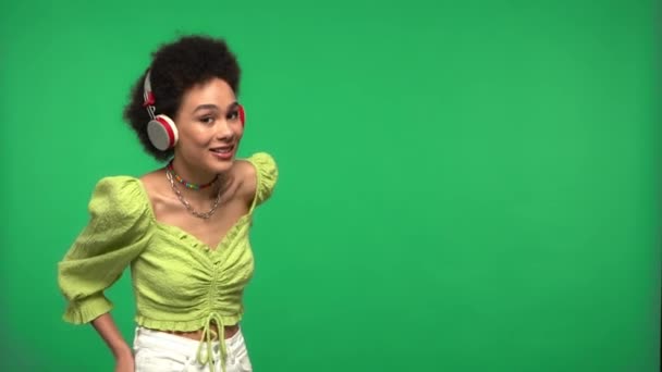 Afrykańska amerykanka używa słuchawek i smartfona odizolowanych na zielono - Materiał filmowy, wideo
