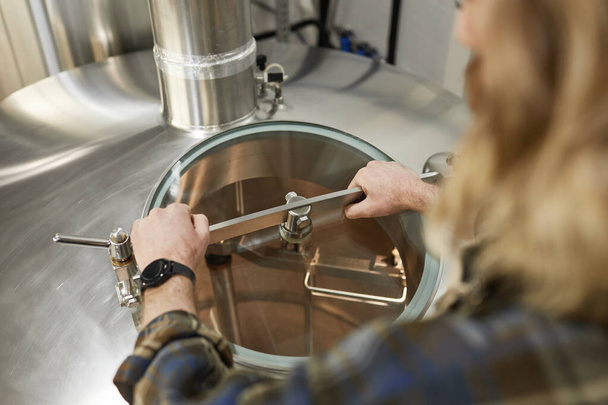 Alto ângulo de perto dos tanques de abertura do trabalhador masculino na cervejaria, processo de fabricação de cerveja, espaço de cópia - Foto, Imagem