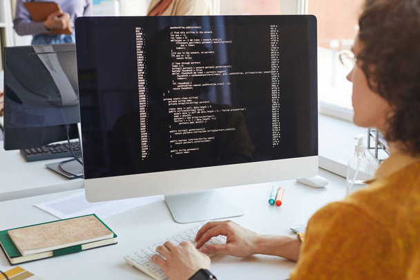 Primer plano del joven desarrollador de TI escribiendo código en la pantalla de la computadora mientras trabaja en el estudio de producción de software, espacio de copia - Foto, Imagen