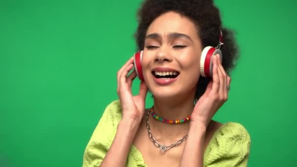 Αφροαμερικανή γυναίκα με ακουστικά που τραγουδά απομονωμένη στο πράσινο  - Πλάνα, βίντεο