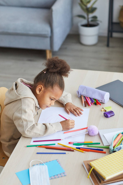 High angle portrait of cute African-American girl drawing pictures while sitting at desk in cozy home interior, copy space - Φωτογραφία, εικόνα