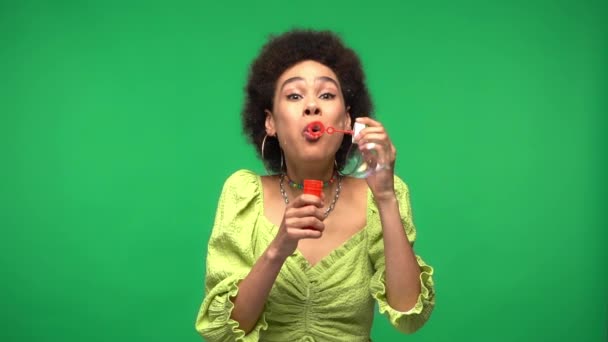 Грустная африканская американка, пускающая мыльные пузыри, изолированные на зеленом  - Кадры, видео