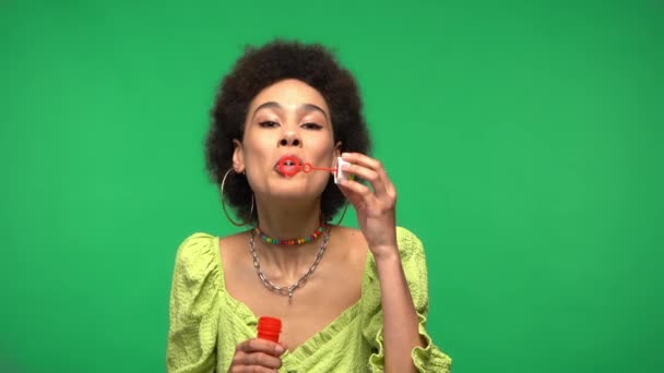 rizado africano americano mujer soplando jabón burbujas aislado en verde  - Imágenes, Vídeo