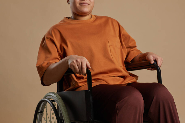 Cropped portrait of contemporary mixed race woman using wheelchair while posing in studio against neutral background - Photo, Image