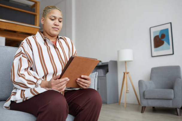 Low angle portrait of modern mixed-race woman holding digital tablet while using online app at home, copy space - Valokuva, kuva