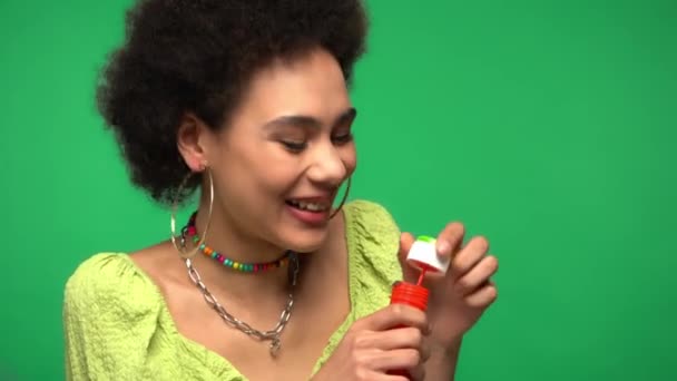 Riendo mujer afroamericana soplando burbujas de jabón aisladas en verde  - Metraje, vídeo