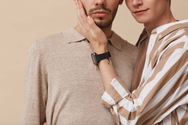 Cropped portrait of young gay couple embracing gently while posing against beige background in studio, copy space - Photo, Image