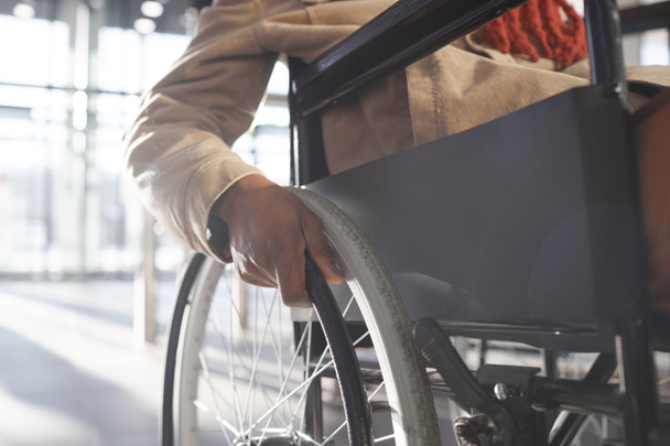 Κοντινό πλάνο αγνώριστου Αφροαμερικανού που χρησιμοποιεί αναπηρικό καροτσάκι κατά τη μεταφορά του στην αστική πόλη, με έμφαση στο χέρι στο τιμόνι, αντιγραφή χώρου - Φωτογραφία, εικόνα